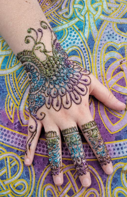 Multicoloured glitter henna peacock covering a hand with banded fingers