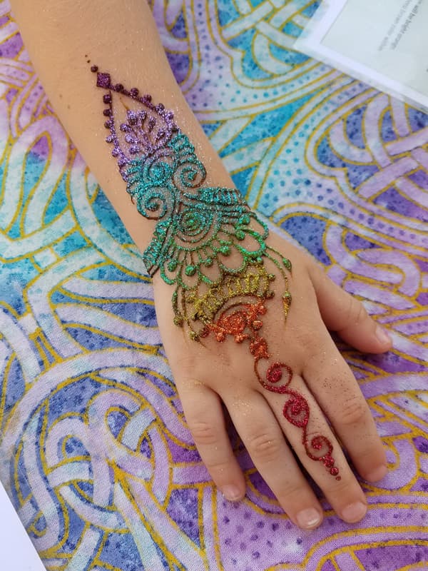 Rainbow glitter henna design shading from purple to red across a hand