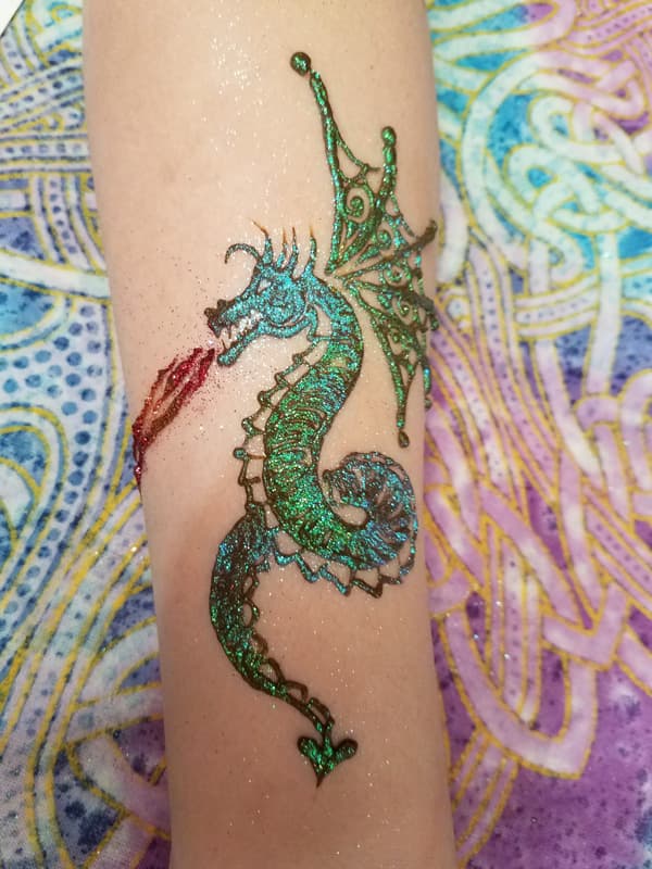 Green and teal glitter henna seahorse on a forearm