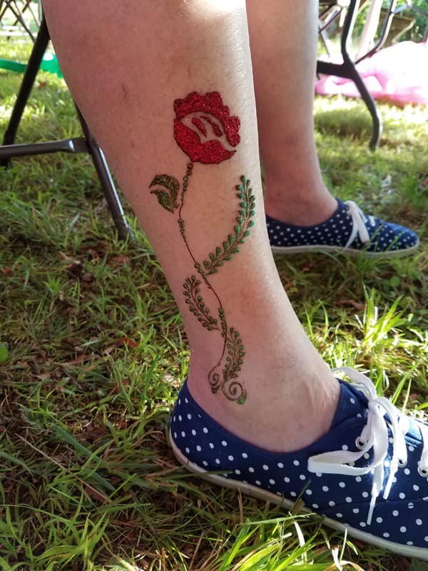 Red and green glitter henna rose with a trailing stem on a lower leg