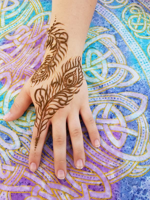 Two henna peacock feathers spreading across the back of a hand