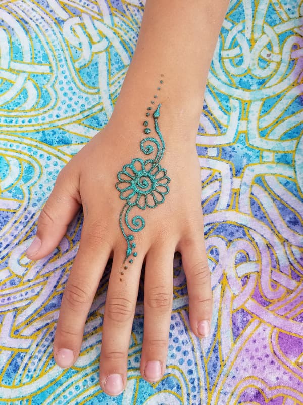 Teal glitter henna flower and vine on a child's hand