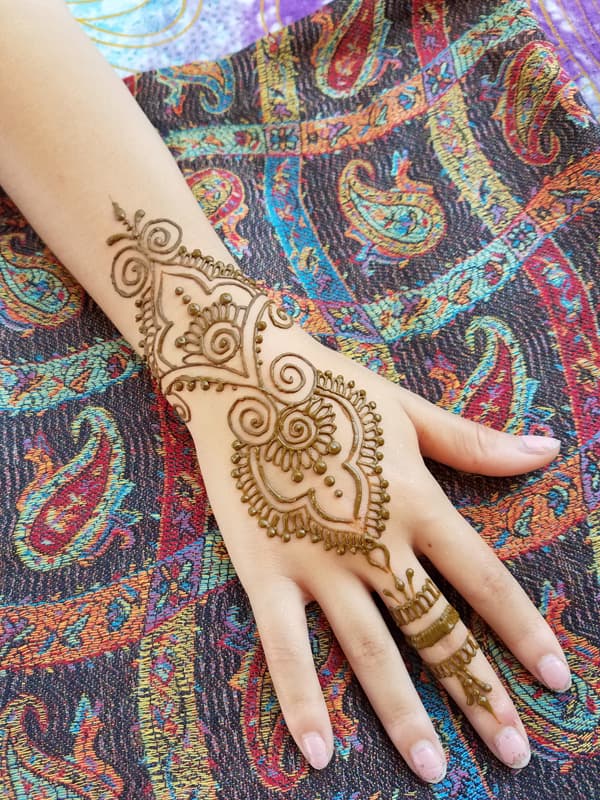 Swirling henna paisley design on the back of a hand with a banded finger
