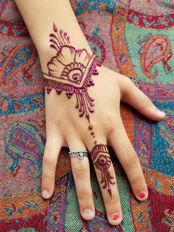 Magenta glitter henna shell design with dangling beads across a hand