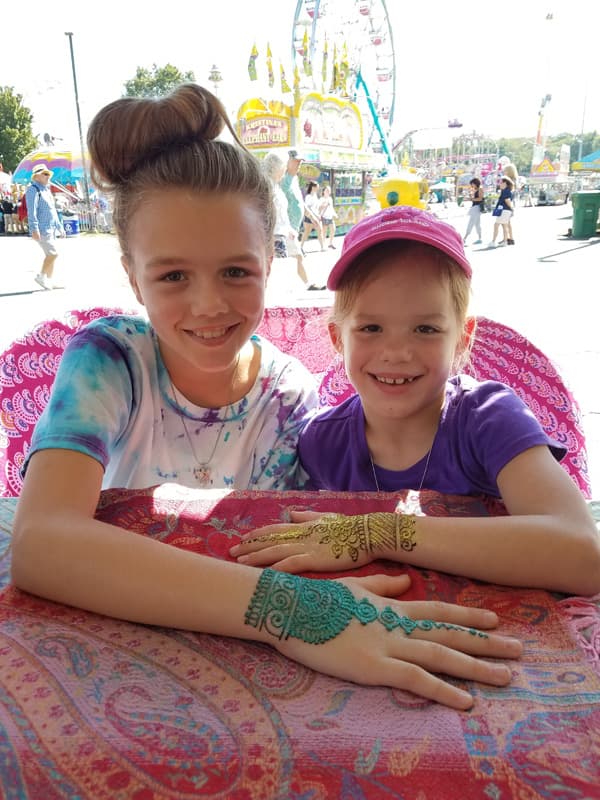 Two young sisters at a fair showing off their gold and teal glitter henna