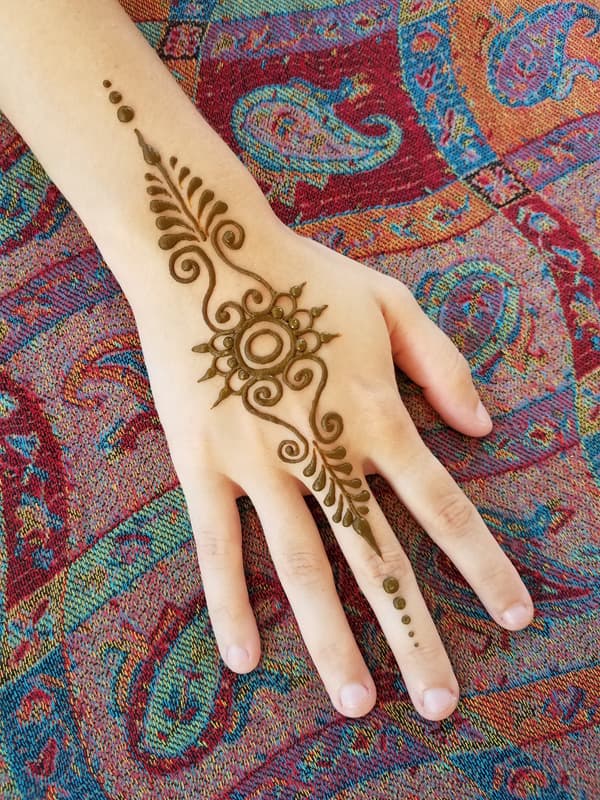 Henna vine and sunburst design running the length of a hand and middle finger