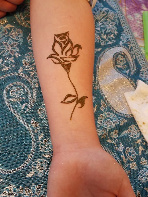 Simple outlined henna rose with a long stem on a forearm