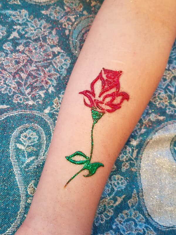 Red and green glitter henna rose on a forearm
