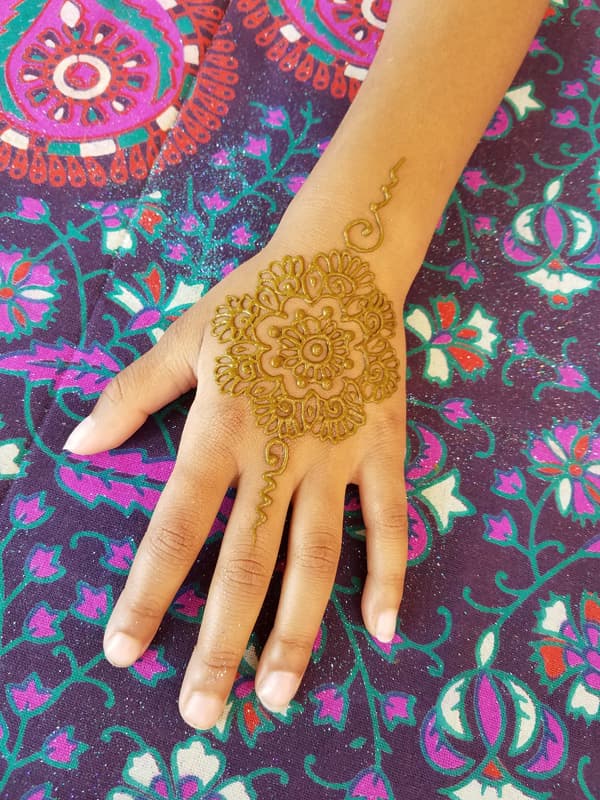 Henna flower medallion on the back of a hand against a bright floral cloth