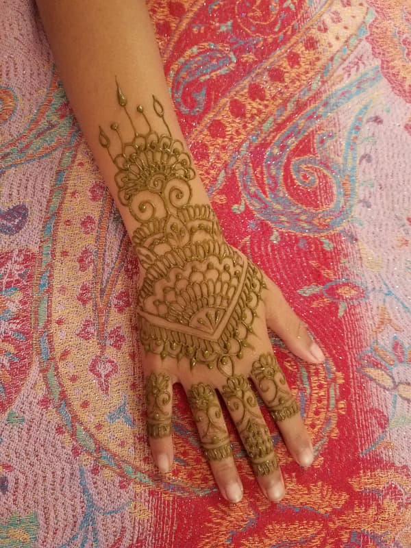 Layered fan and petal henna design covering the back of a hand and fingers