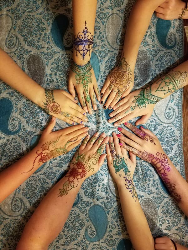 Ten hands arranged in a circle, each with a different coloured henna design