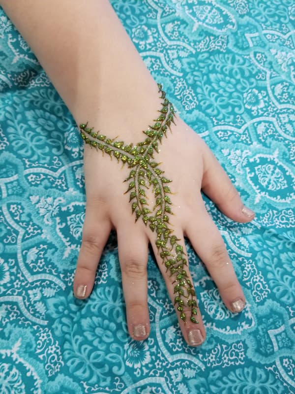 Green glitter henna vine forming a bracelet and finger chain on a child's hand