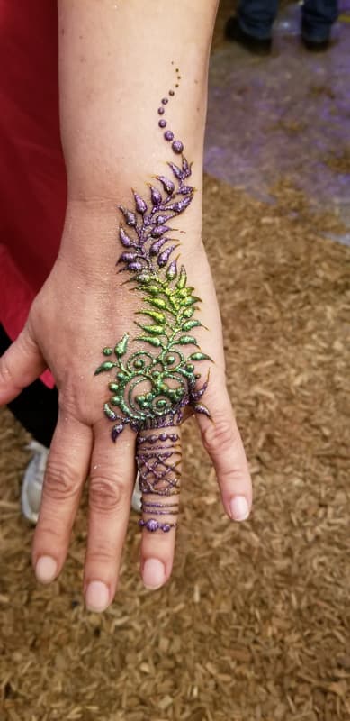 Purple and green glitter henna leaf climbing the back of a hand and one finger
