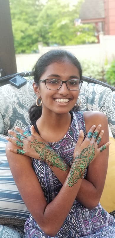 Guest with green glitter henna trailing across her crossed hands and arms