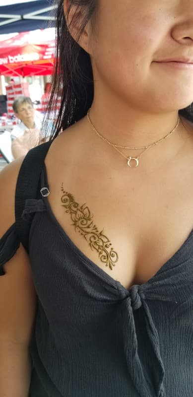 Flowing henna floral design along a guest's collarbone and shoulder