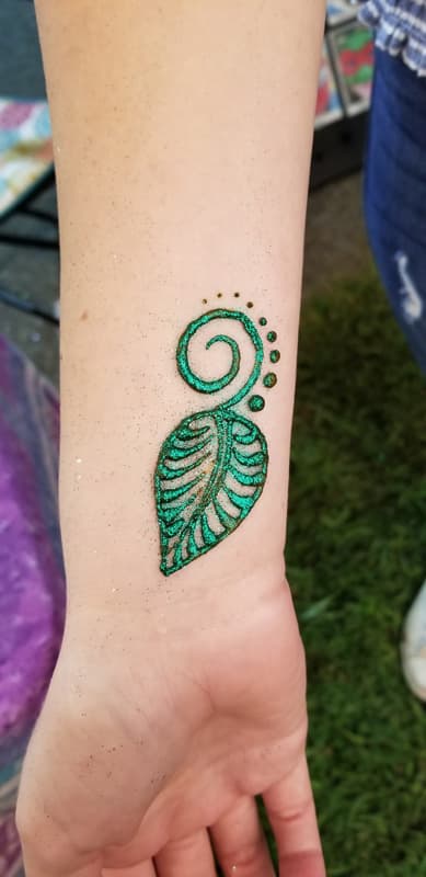 Green glitter henna leaf and spiral on the inside of a forearm
