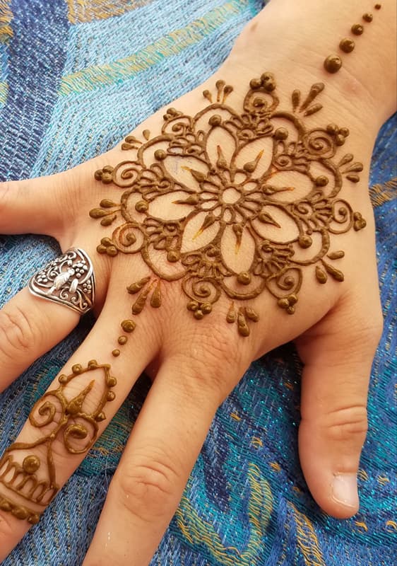 Bold henna flower mandala on the back of a hand with a decorated finger