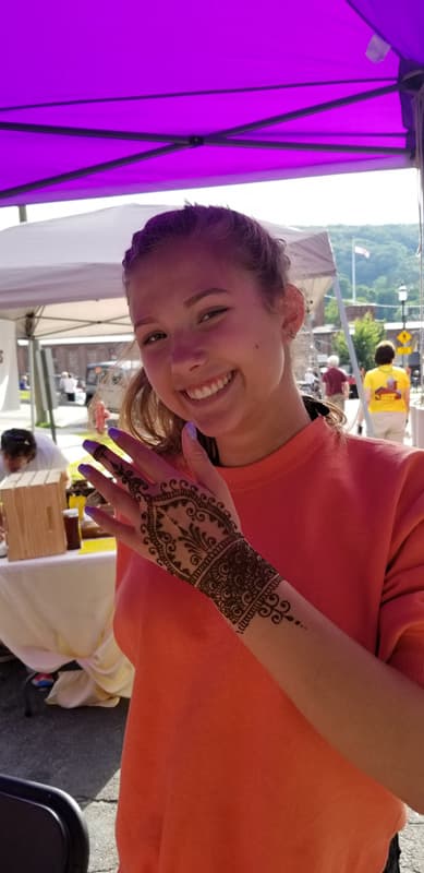 Guest at an outdoor market smiling beside her fresh henna hand design